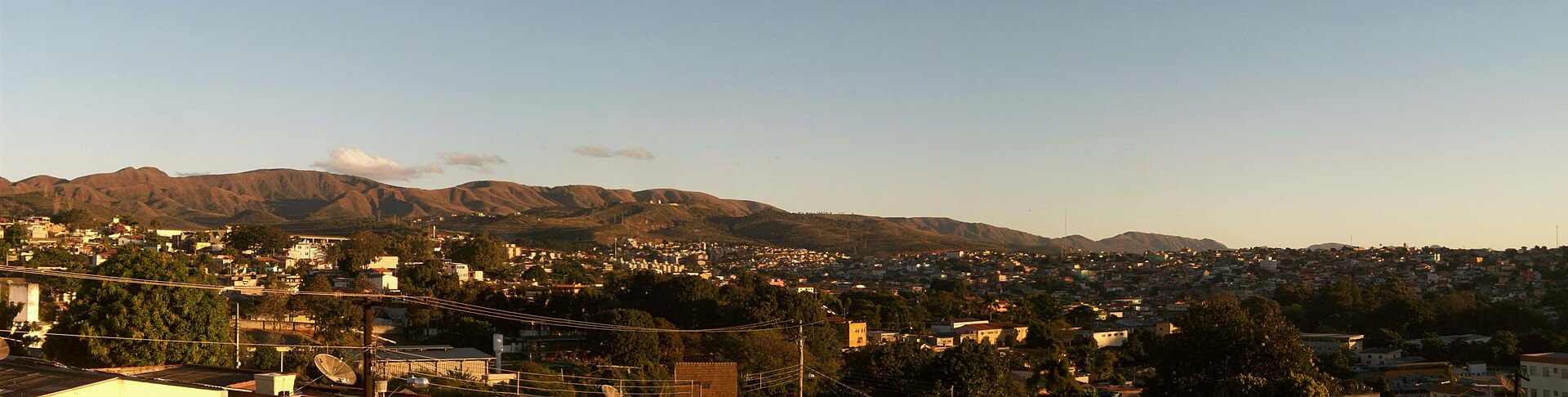 Vista do Barreiro de Cima, em Belo Horizonte, com casas e árvores em primeiro plano e a serra ao fundo no fim da tarde