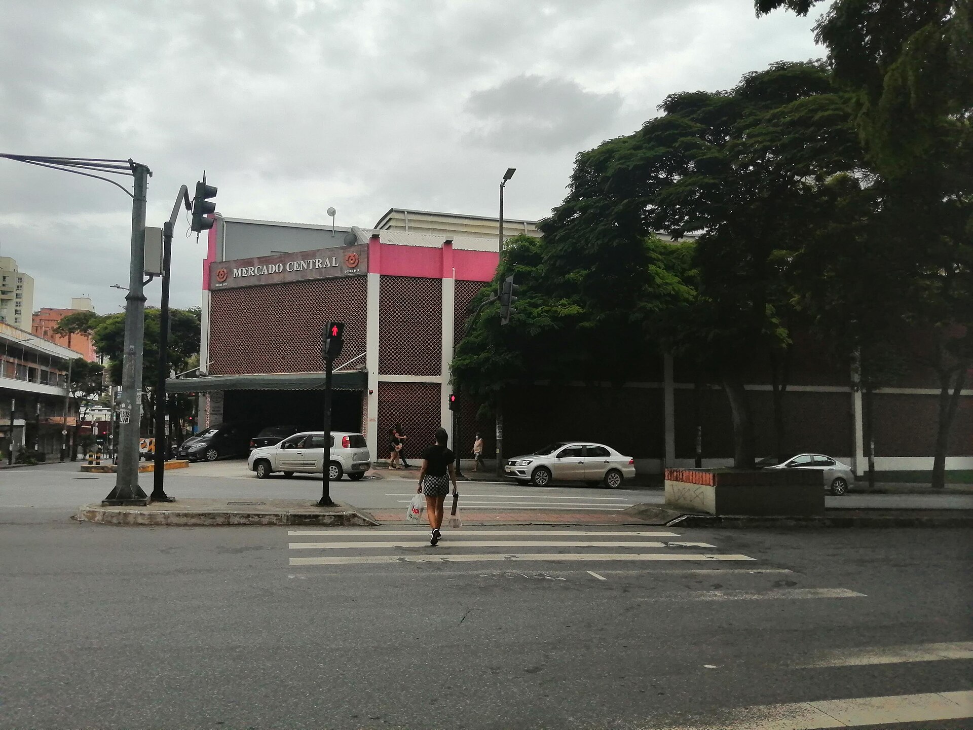 Fachada do Mercado Central, no Centro de Belo Horizonte, com o letreiro no alto, a faixa de pedestres em frente e árvores na calçada